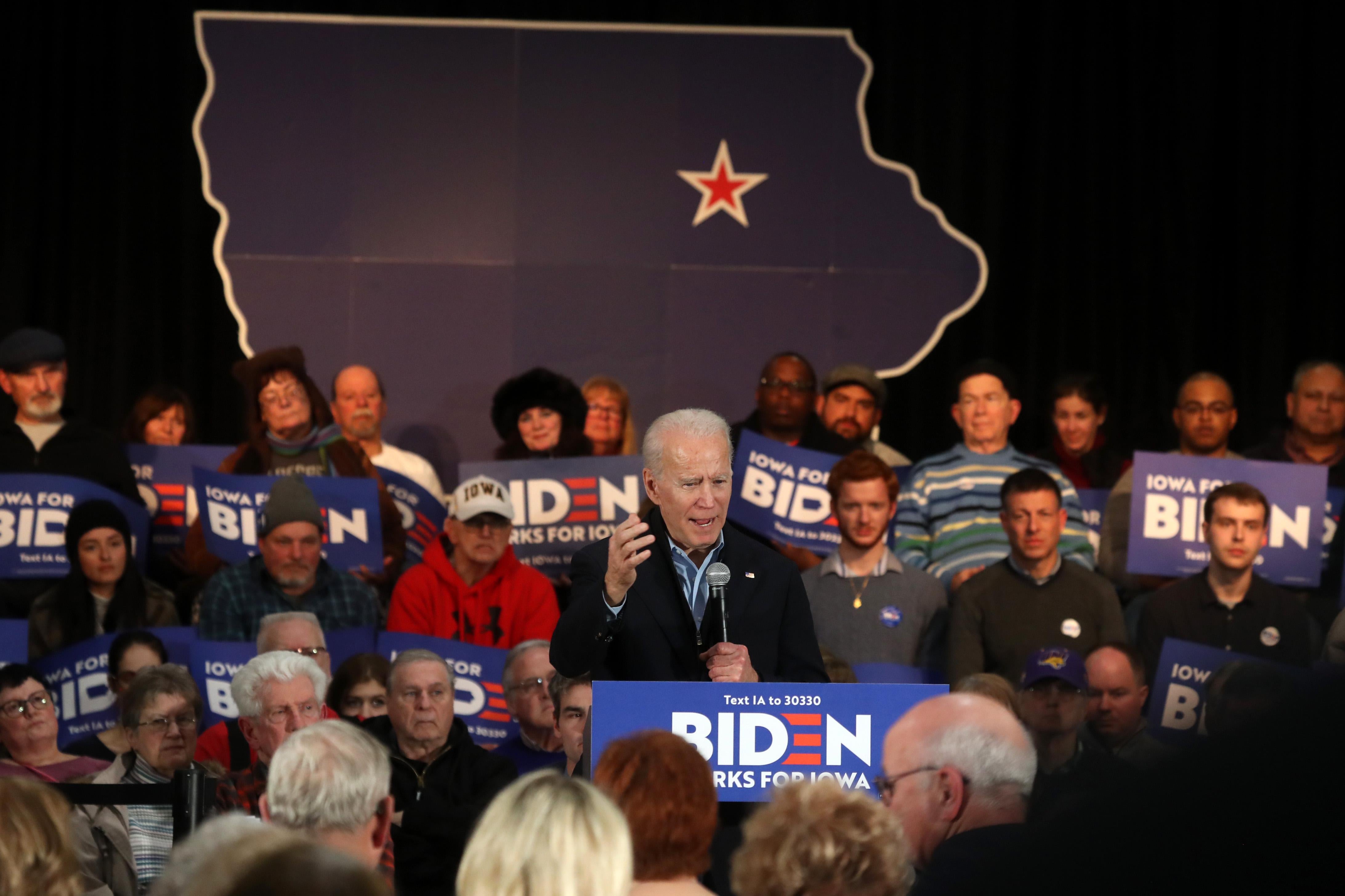 Biden speaks surrounded by "Biden Works for Iowa" signs. Behind him is an outline of the U.S., with a star over Iowa.