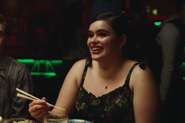 A girl with black hair sits at a table holding chopsticks and smiles.