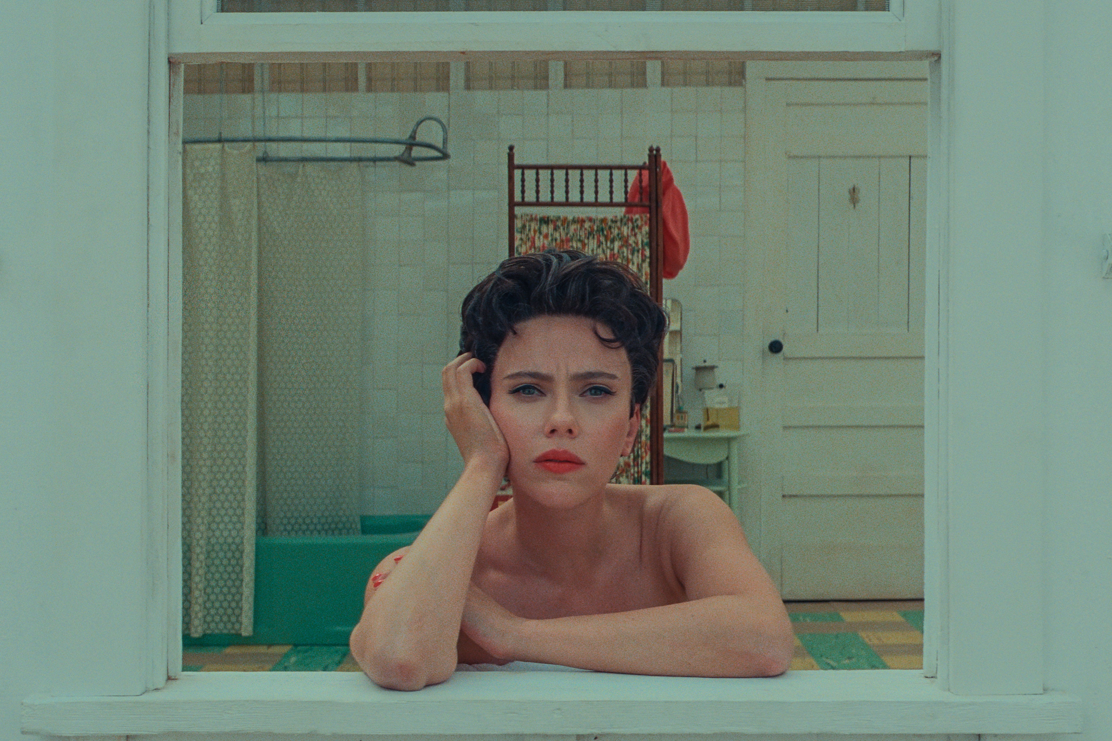 Scarlett Johansson looks pensively out a bathroom window as her character Midge in Asteroid City.