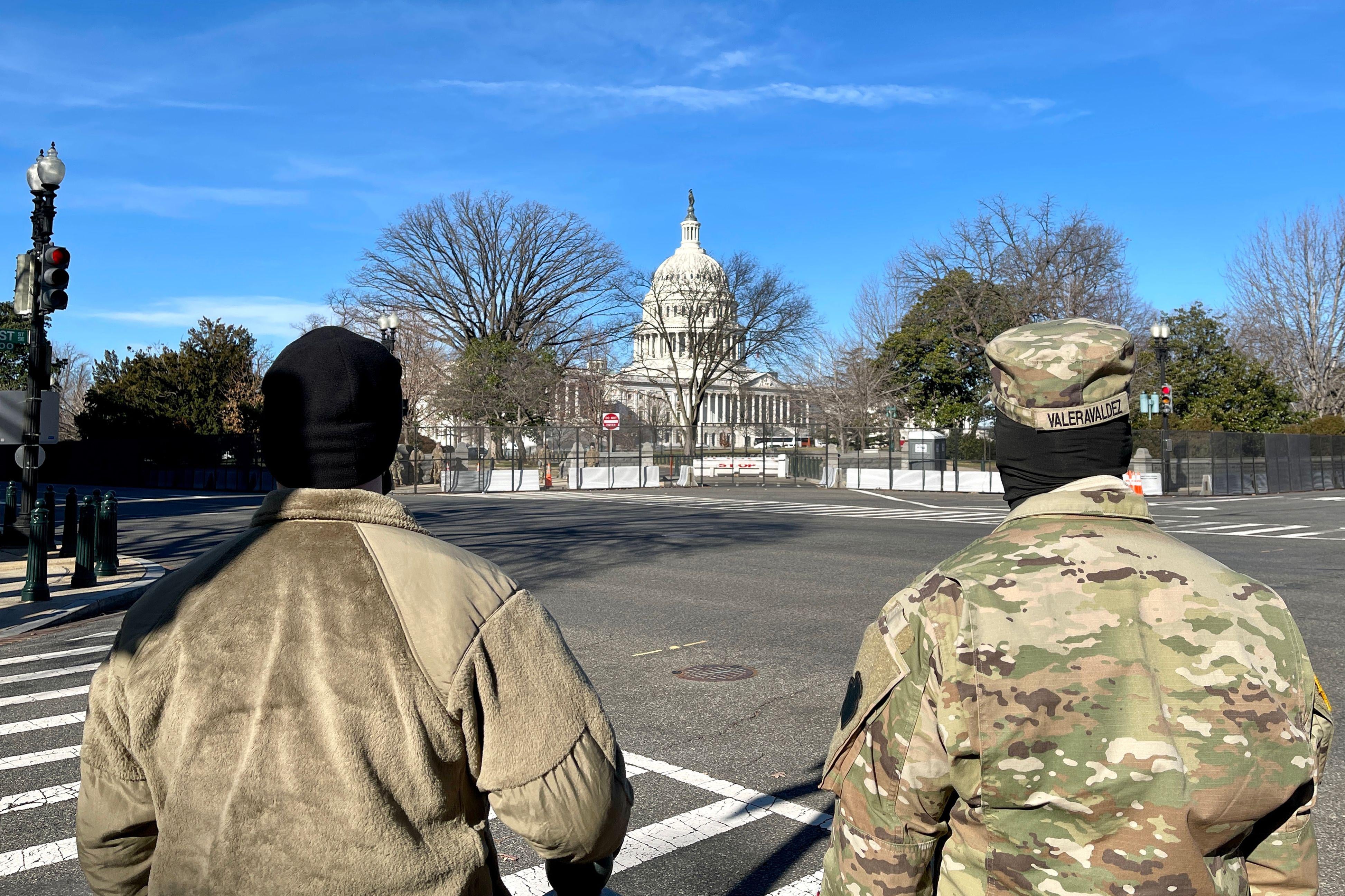 Two National Guard members seen from the back, standing in an intersection, as they look toward the Capitol dome and grounds, which are surrounded by a new security fence