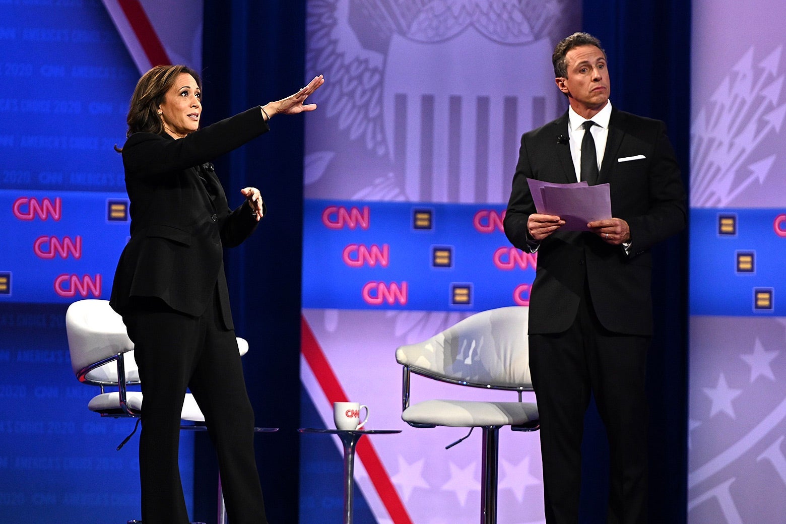 Kamala Harris points out toward the audience as Chris Cuomo stands beside her holding documents.
