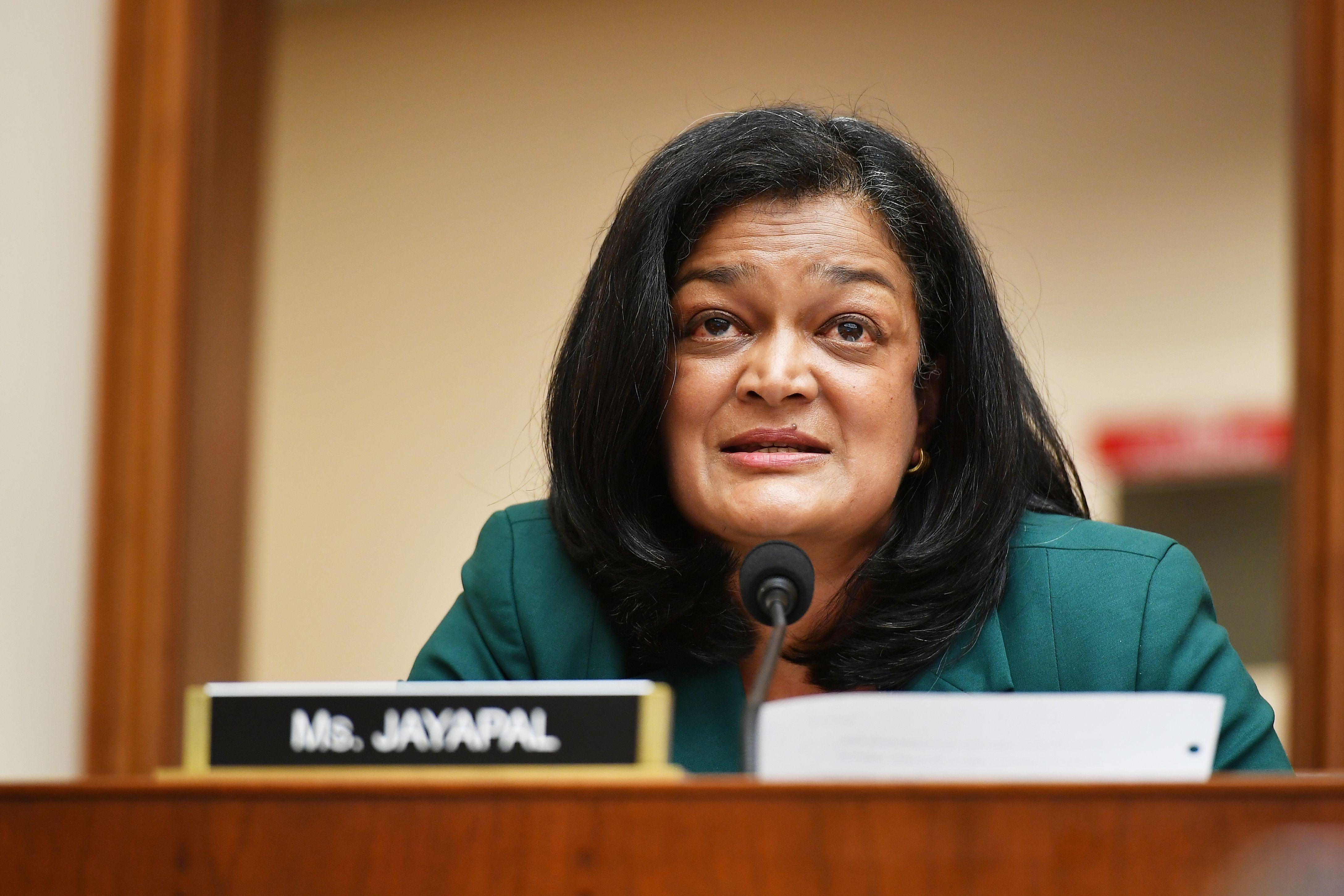 Pramila Jayapal speaks into a microphone. In front of her is a sign that says "Ms. Jayapal."