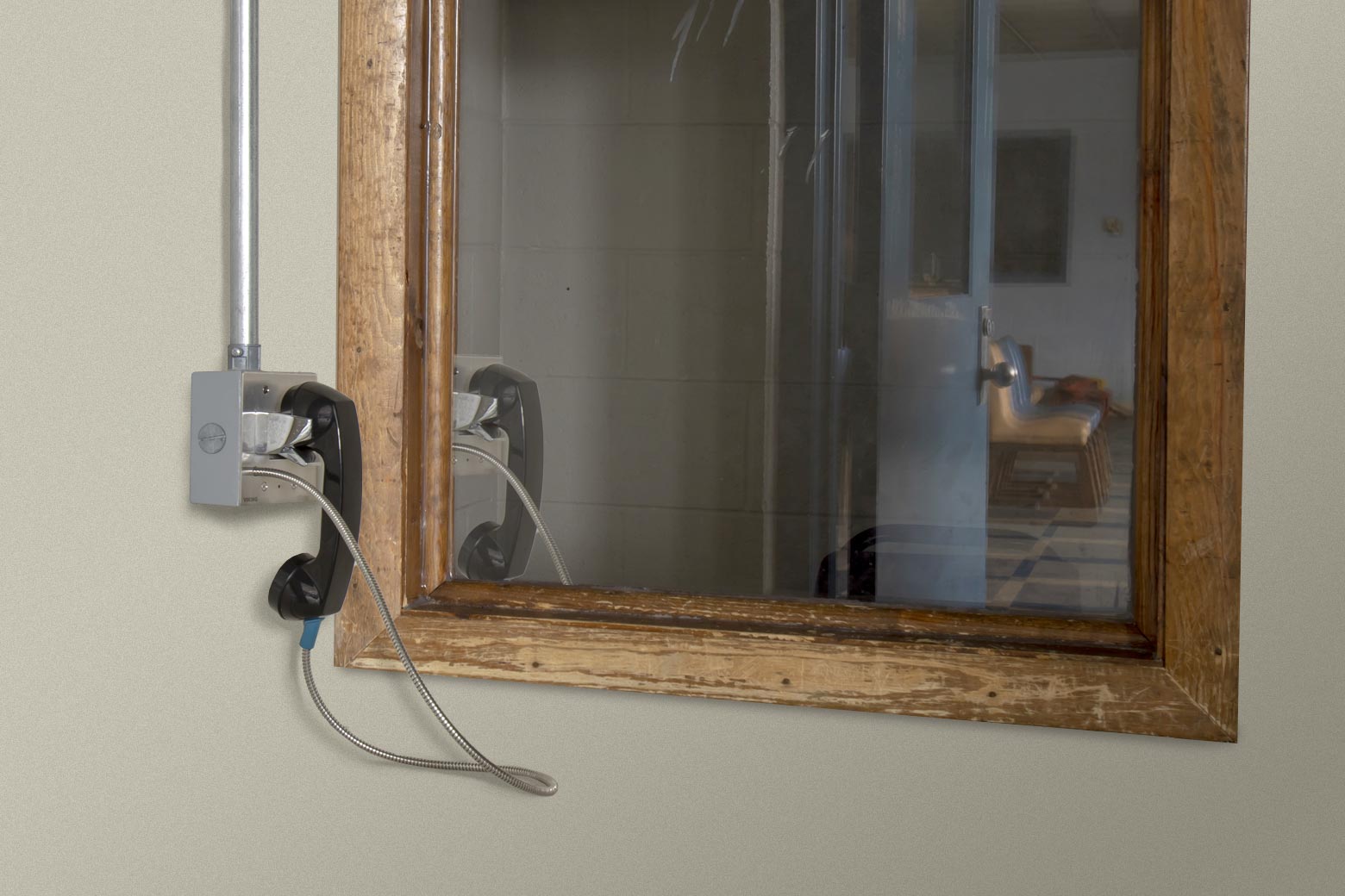 A jail phone hangs in its cradle on one side of a Plexiglas barrier.