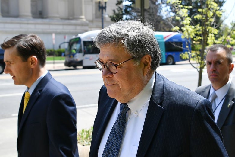 Barr, wearing a suit, walks on a sidewalk with a half-smile on his face.