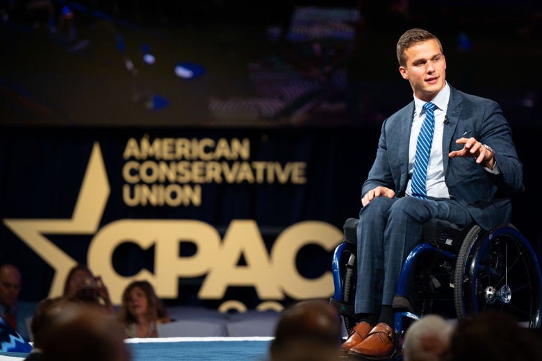 Cawthorn, wearing a blue suit and tie, gestures while speaking onstage in front of a CPAC backdrop.