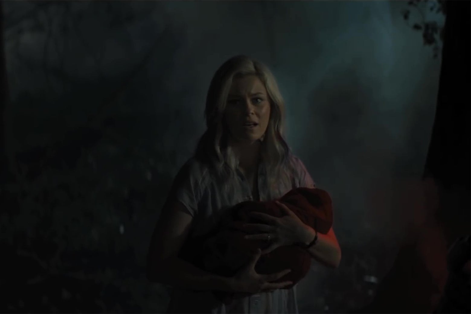 Elizabeth Banks in the middle of the woods, holding a baby wrapped in a red cape. 