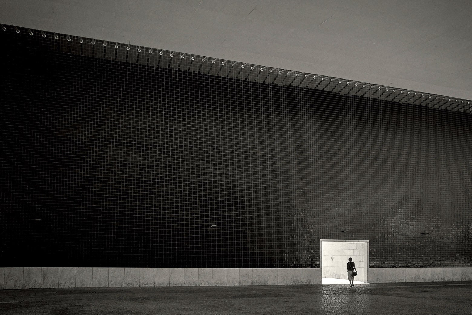 A woman standing alone in a vast, dark, empty hall.