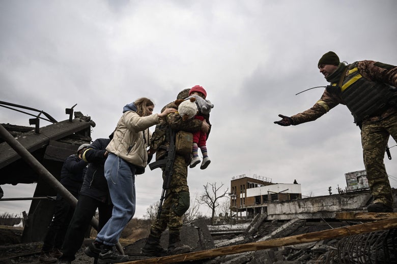 Three people in single file hold onto a Ukrainian service member carrying a child across a destroyed bridge toward another service member extending his hand