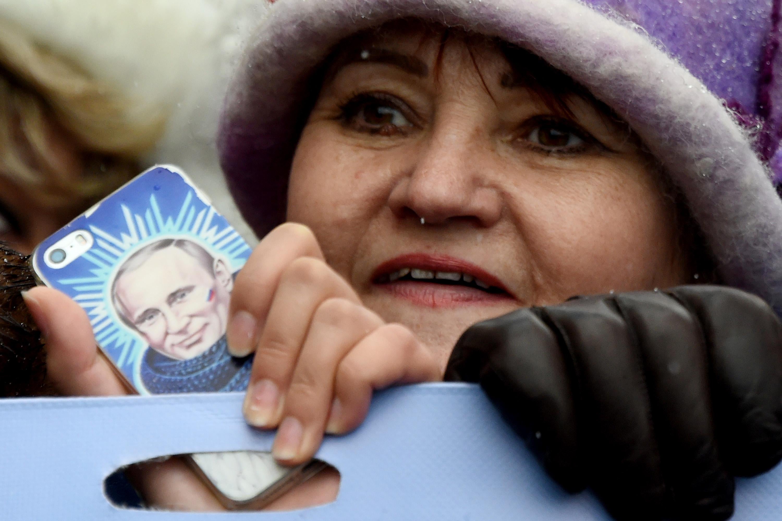 A woman holds a smartphone bearing an image of Russian President Vladimir Putin.