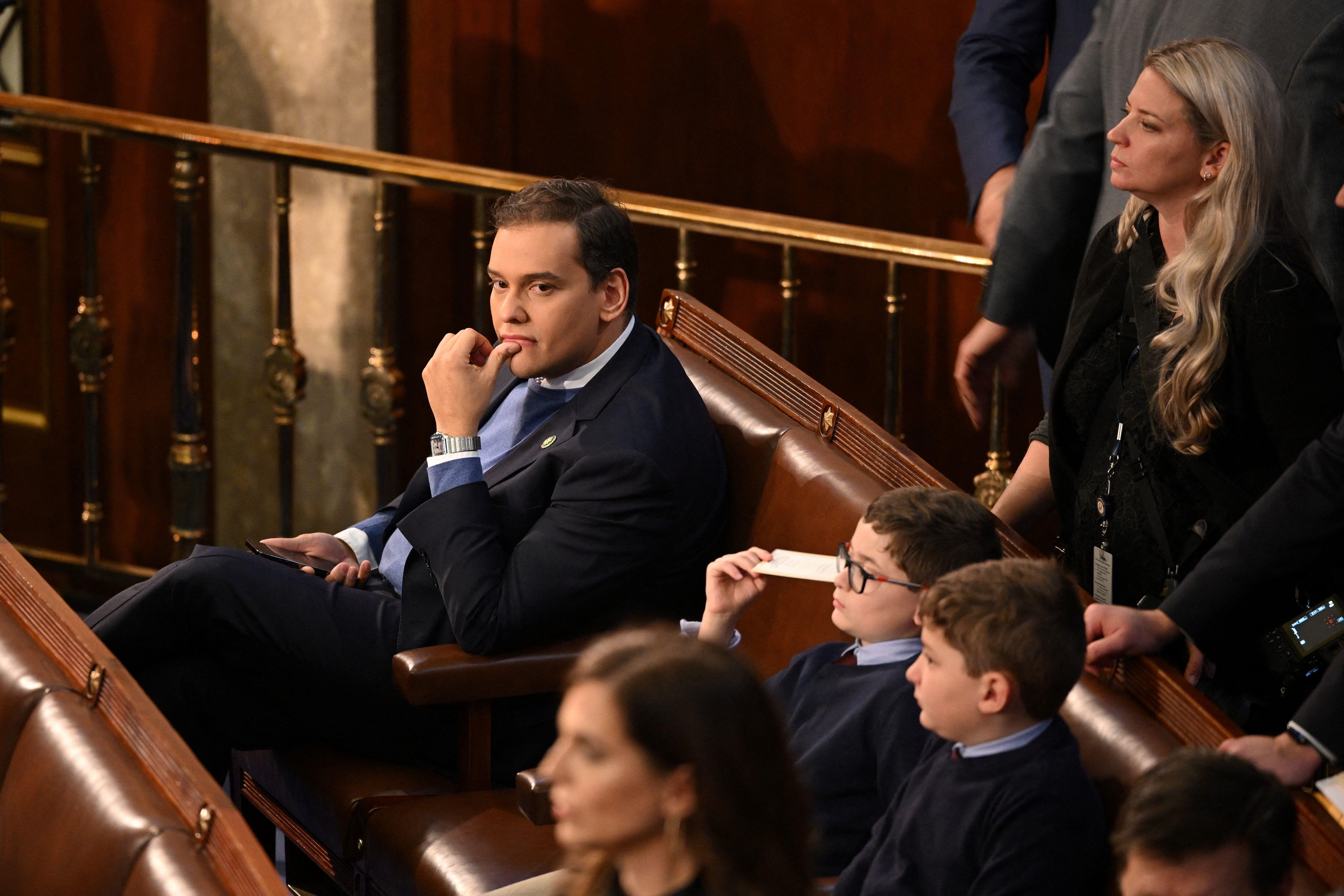 George Santos, an incoming House rep. from New York who lied about nearly every aspect of his background and biography, looking around, nestled between empty seats in Congress.