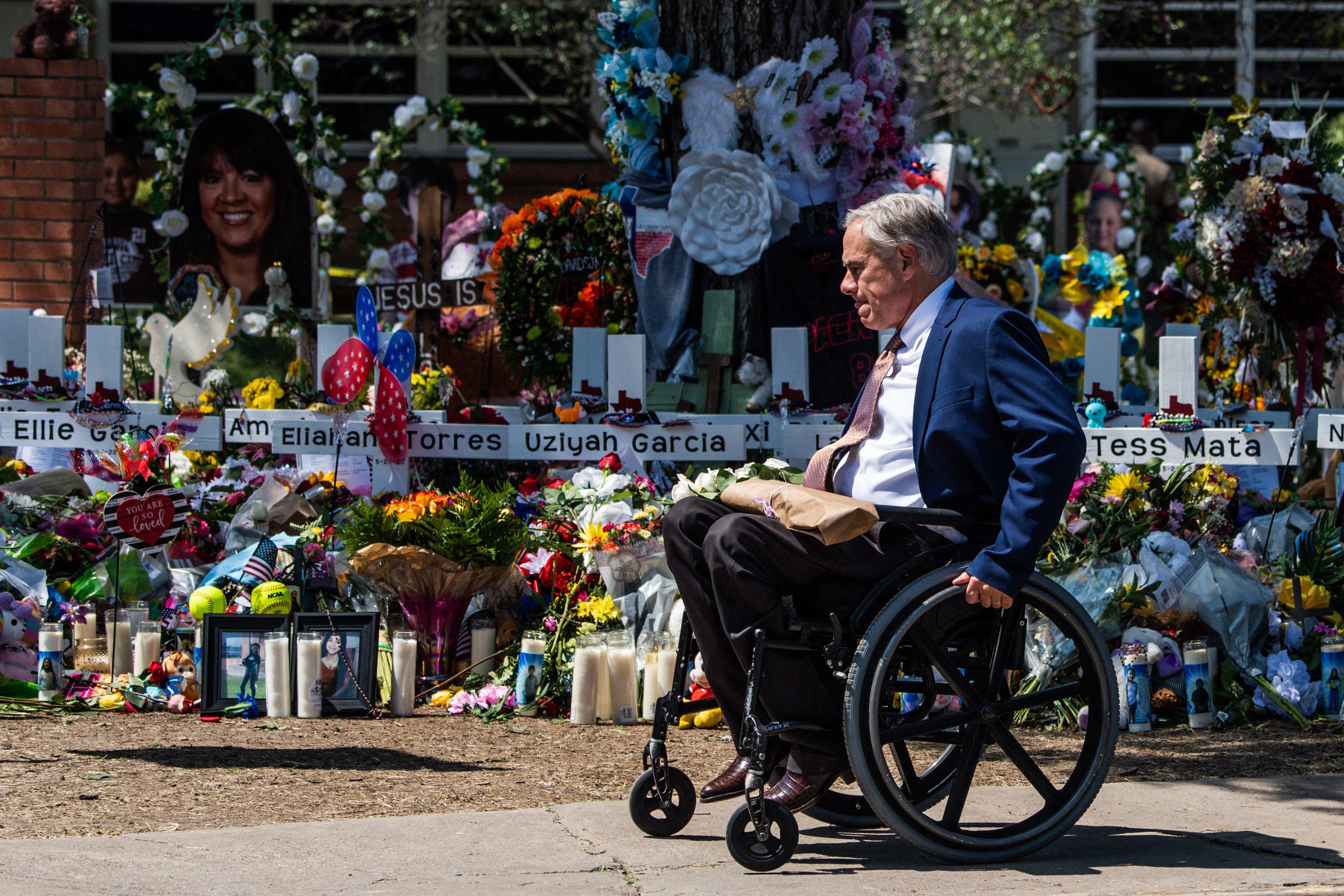 A man in a wheelchair in front of a memorial of candles and flowers outside the elementary school.