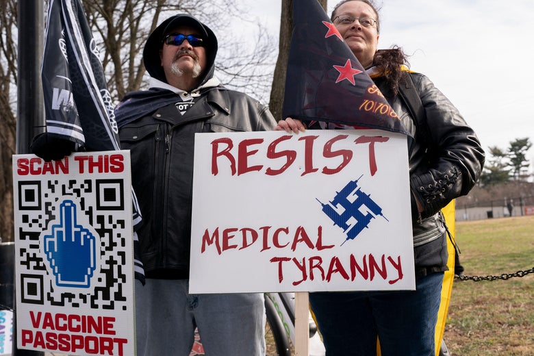 Demonstrators in Washington hold up signs, one with a middle finger and a QR code that reads "SCAN THIS VACCINE PASSPORT" and another with a swastika that reads "RESIST MEDICAL TYRANNY."