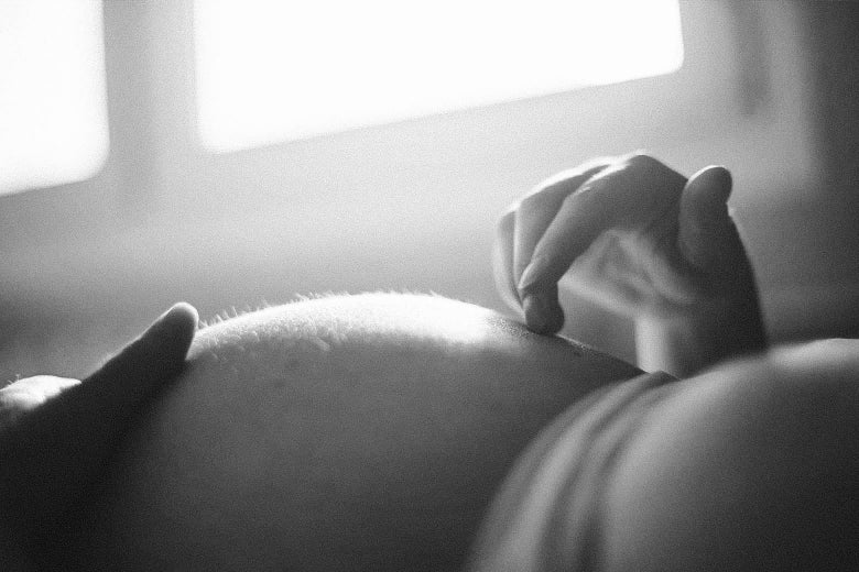 A woman traces her fingers along her pregnant belly in this black and white photo.