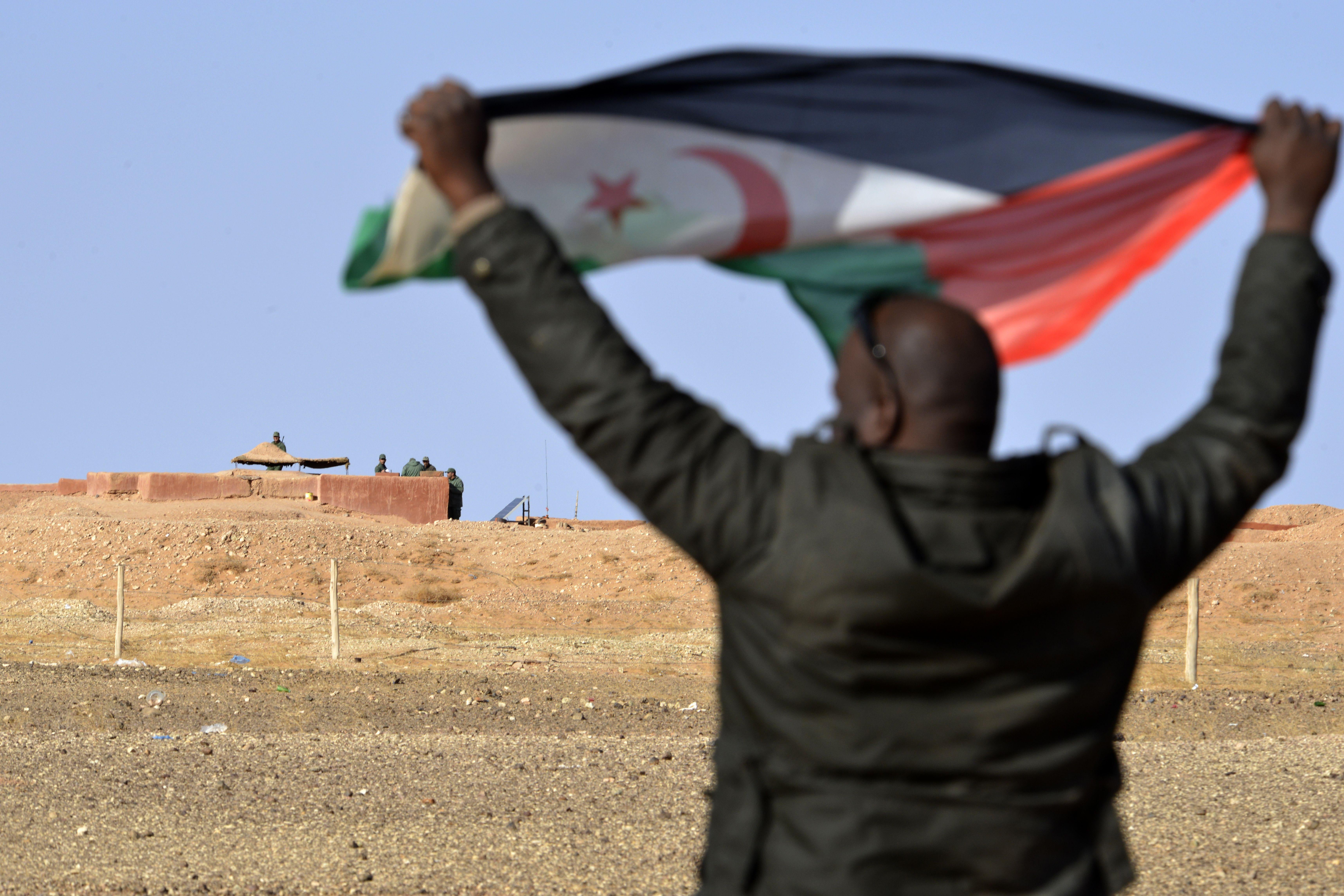 A Saharawi man holds up a Polisario Front flag in the Al-Mahbes area near Moroccan soldiers guarding the wall separating the Polisario controlled Western Sahara from Morocco on February 3, 2017. - It is the world's oldest functioning security barrier, dubbed a wall of "shame" and "death" by Western Sahara residents and leaders who want independence from Morocco. (Photo by STRINGER / AFP) / TO GO WITH AFP STORY BY AMAL BELALLOUFI        (Photo credit should read STRINGER/AFP via Getty Images)