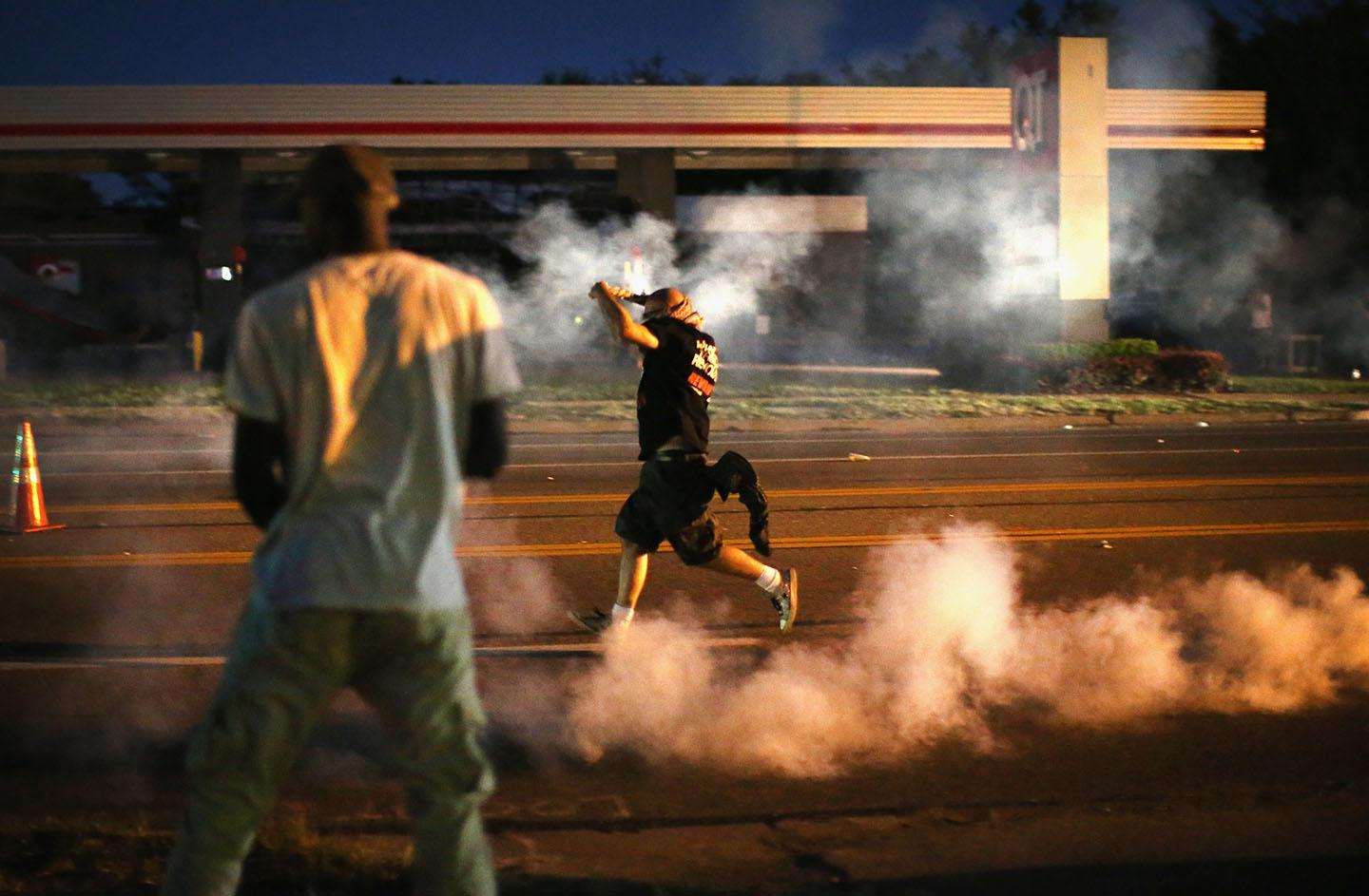 Demonstrators, protesting the shooting death of teenager Michael Brown, scramble for cover as police fire tear gas on August 13, 2014 in Ferguson, Missouri.