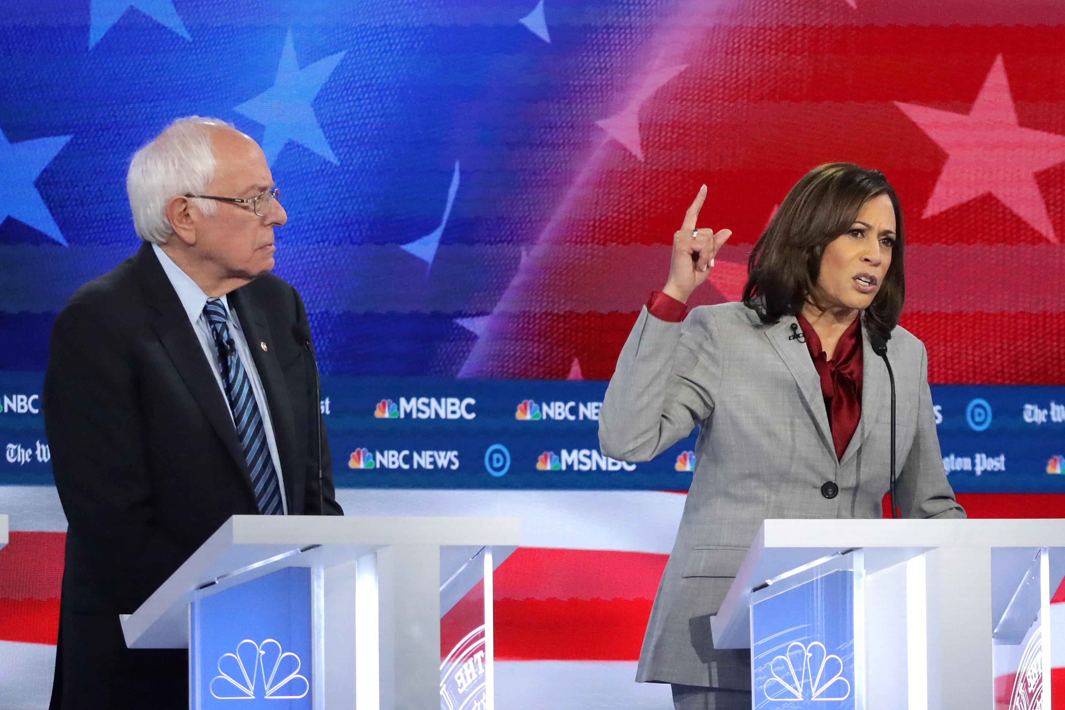 Sanders and Harris stand at lecterns in front of an American flag background.