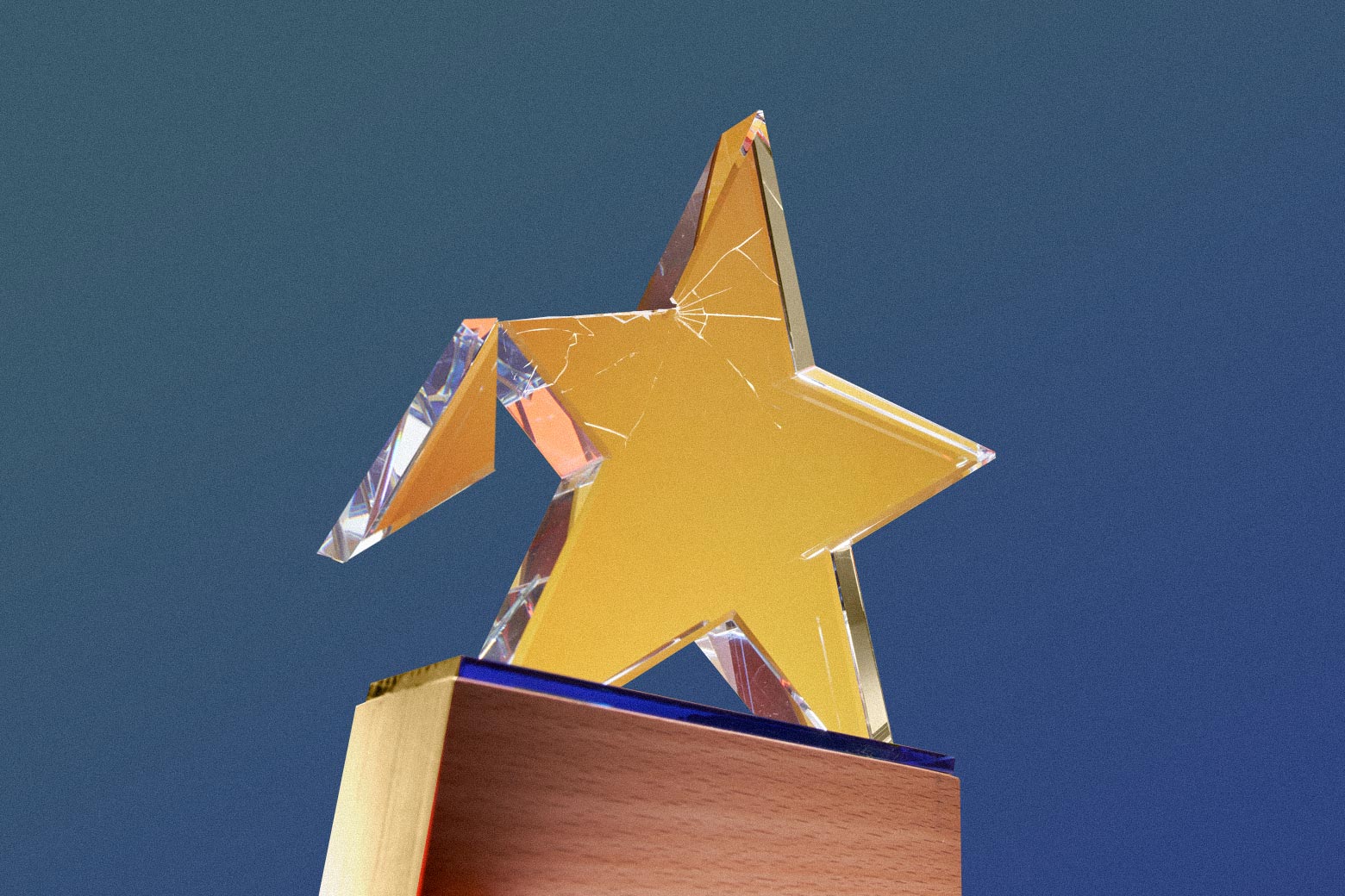 A glass trophy in the shape of a star. The star has a crack in it, and one of the points is falling off. 