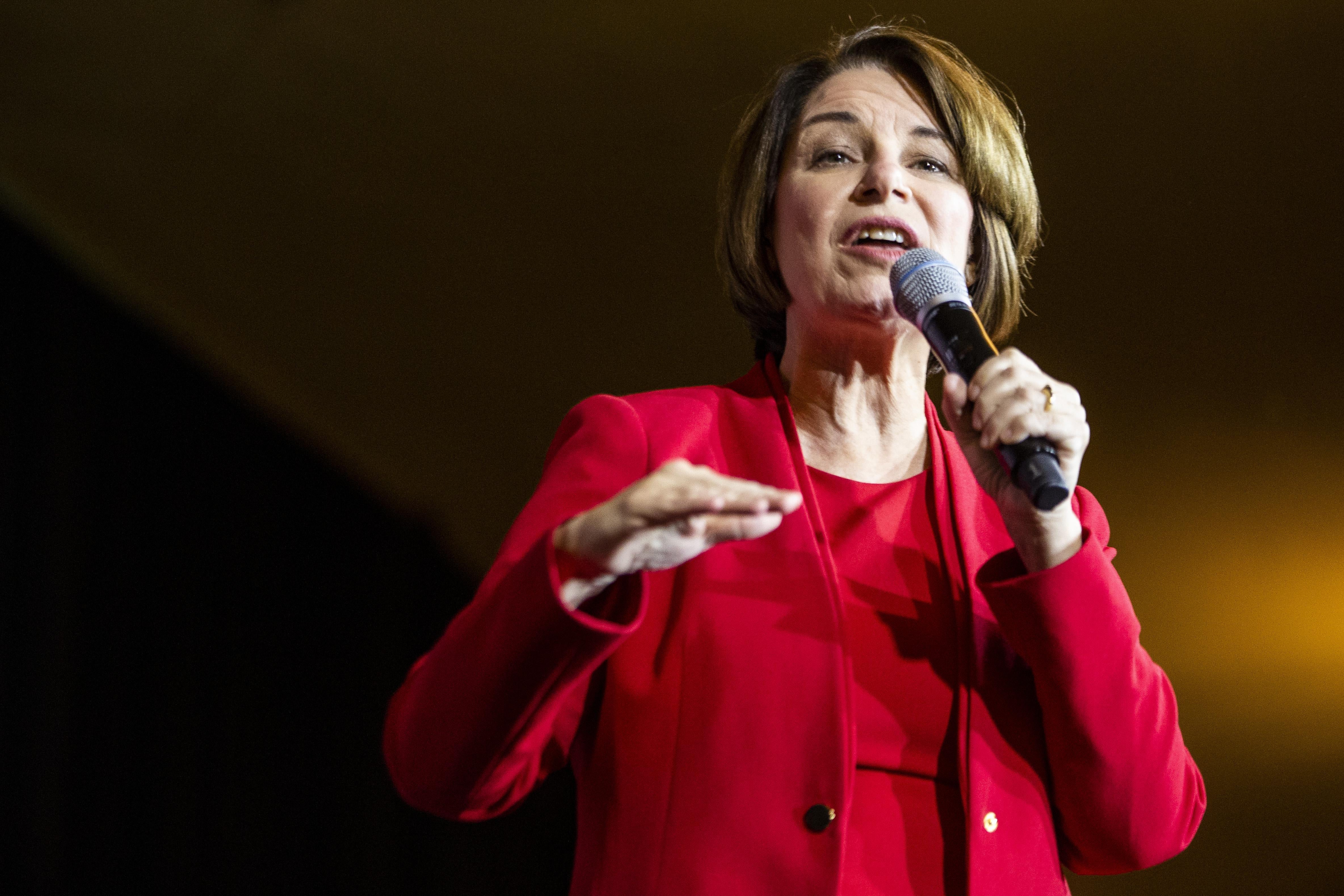 Amy Klobuchar gestures with one hand while holding a microphone in the other.