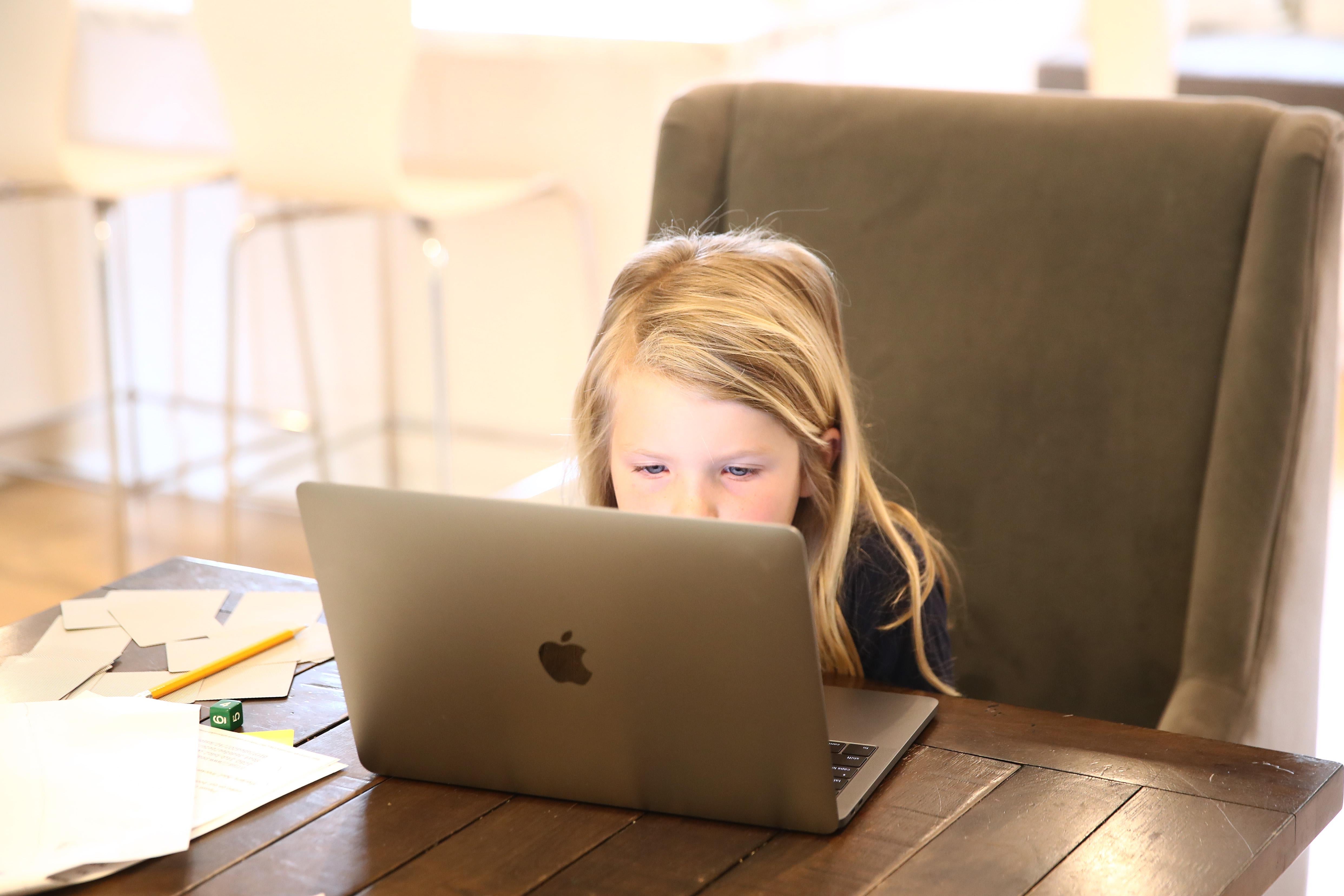 A kindergartener sits at a laptop for remote schooling.