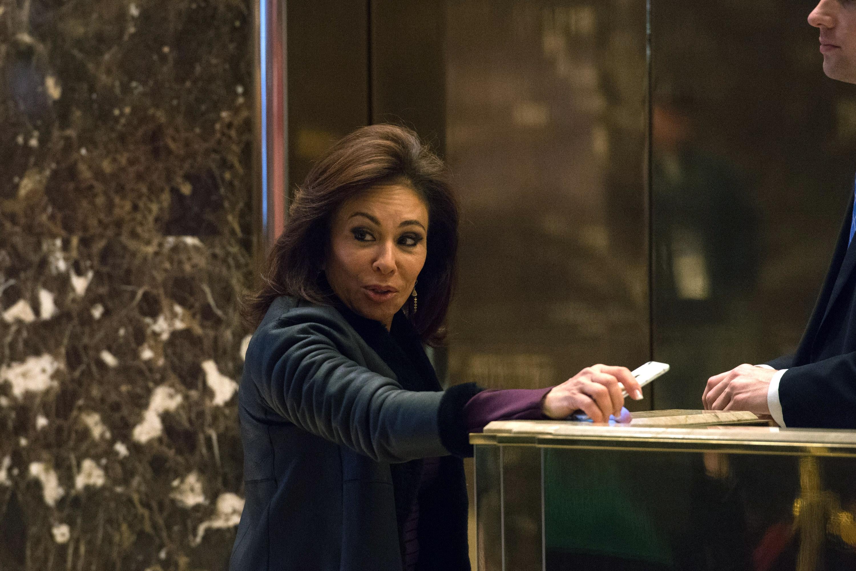 Jeanine Pirro leans against a counter in the lobby, holding her phone