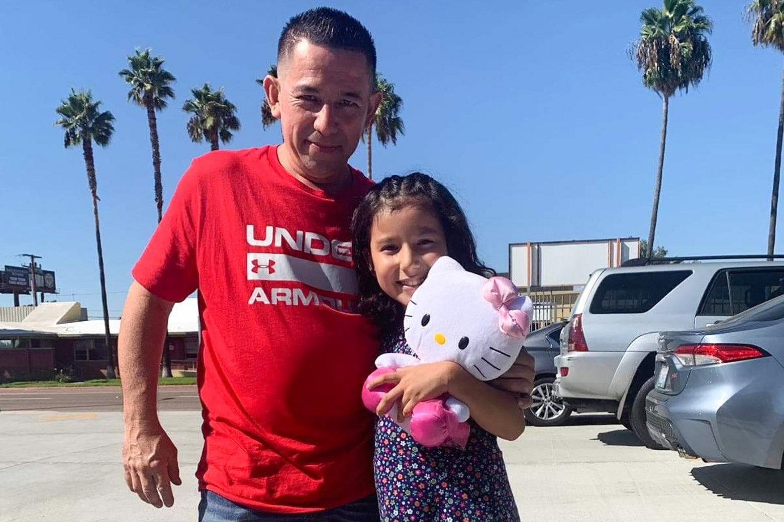 A man stands with his daughter, who is carrying a Hello Kitty toy.
