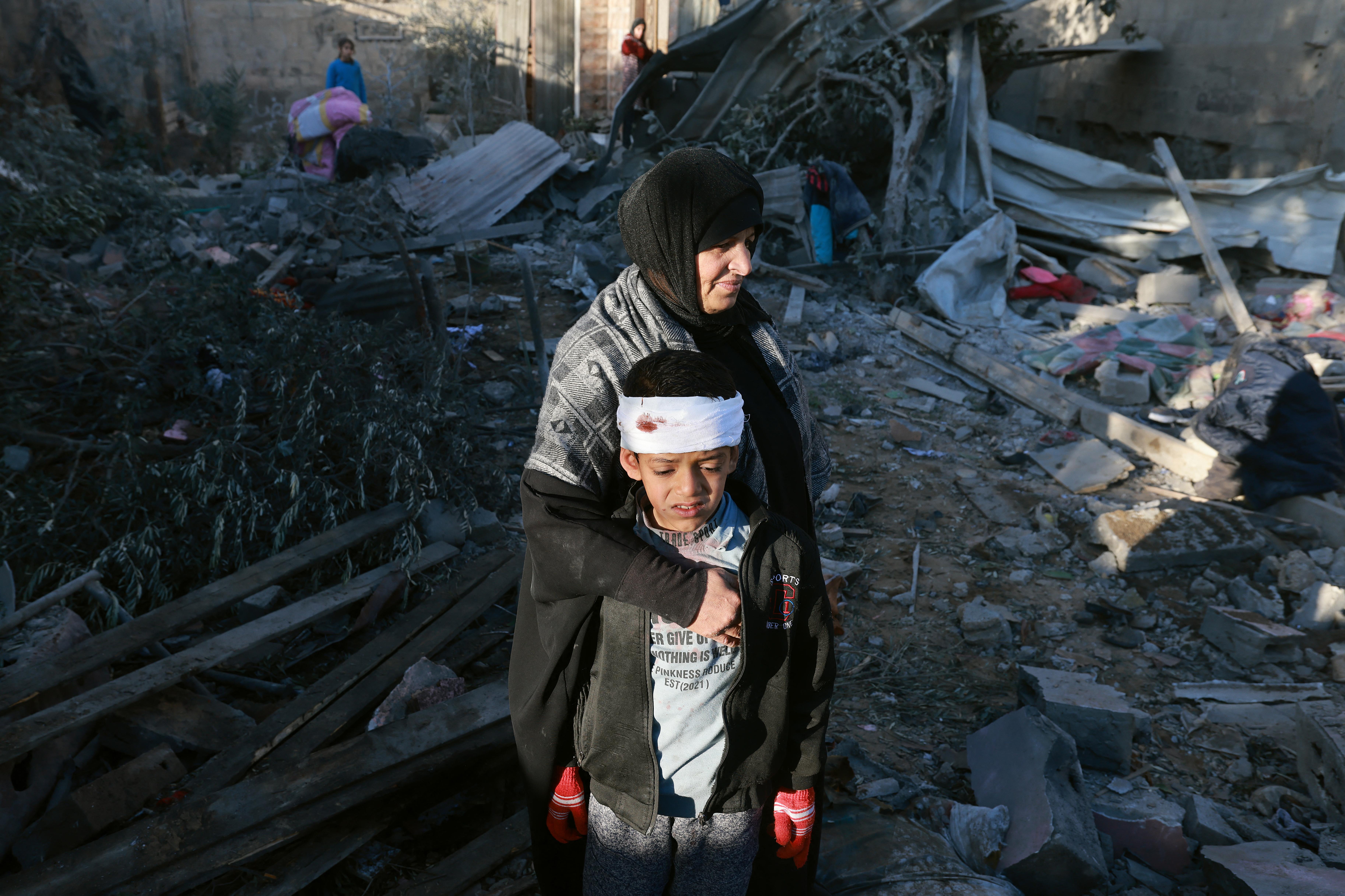 A woman holds her arm around a boy with a bandage on his head.