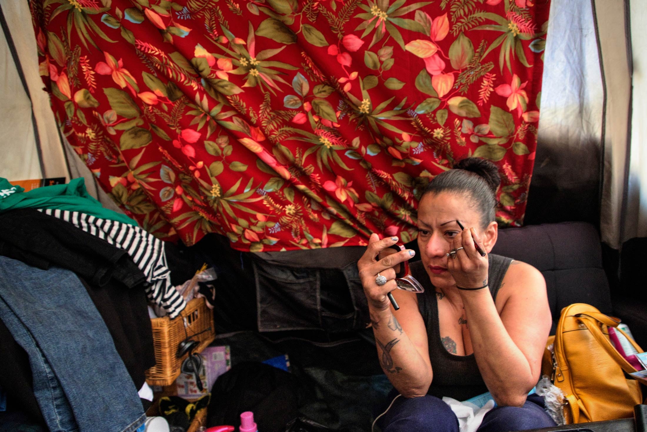Lucrecia Macias applies makeup to her eyebrow while looking in a compact mirror.