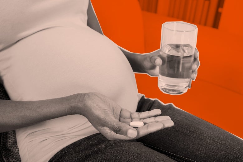 A pregnant woman holds a pill in one hand and a glass of water in the other.