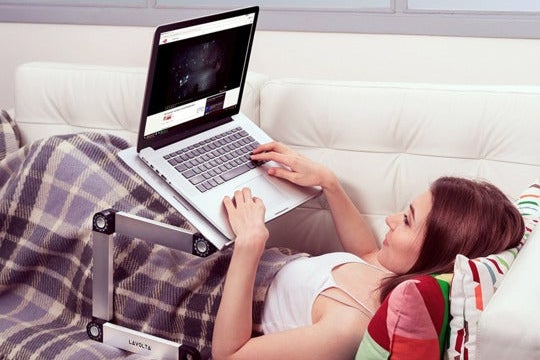 Woman laying on a couch, using a laptop in a stand.