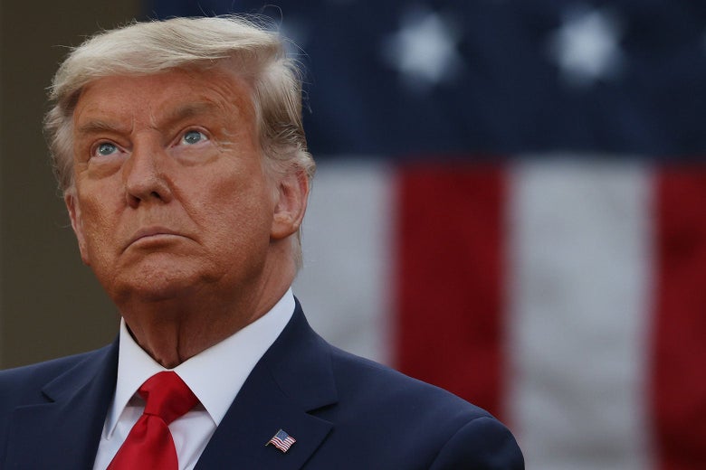 Donald Trump looks up while standing in front of a U.S. flag.