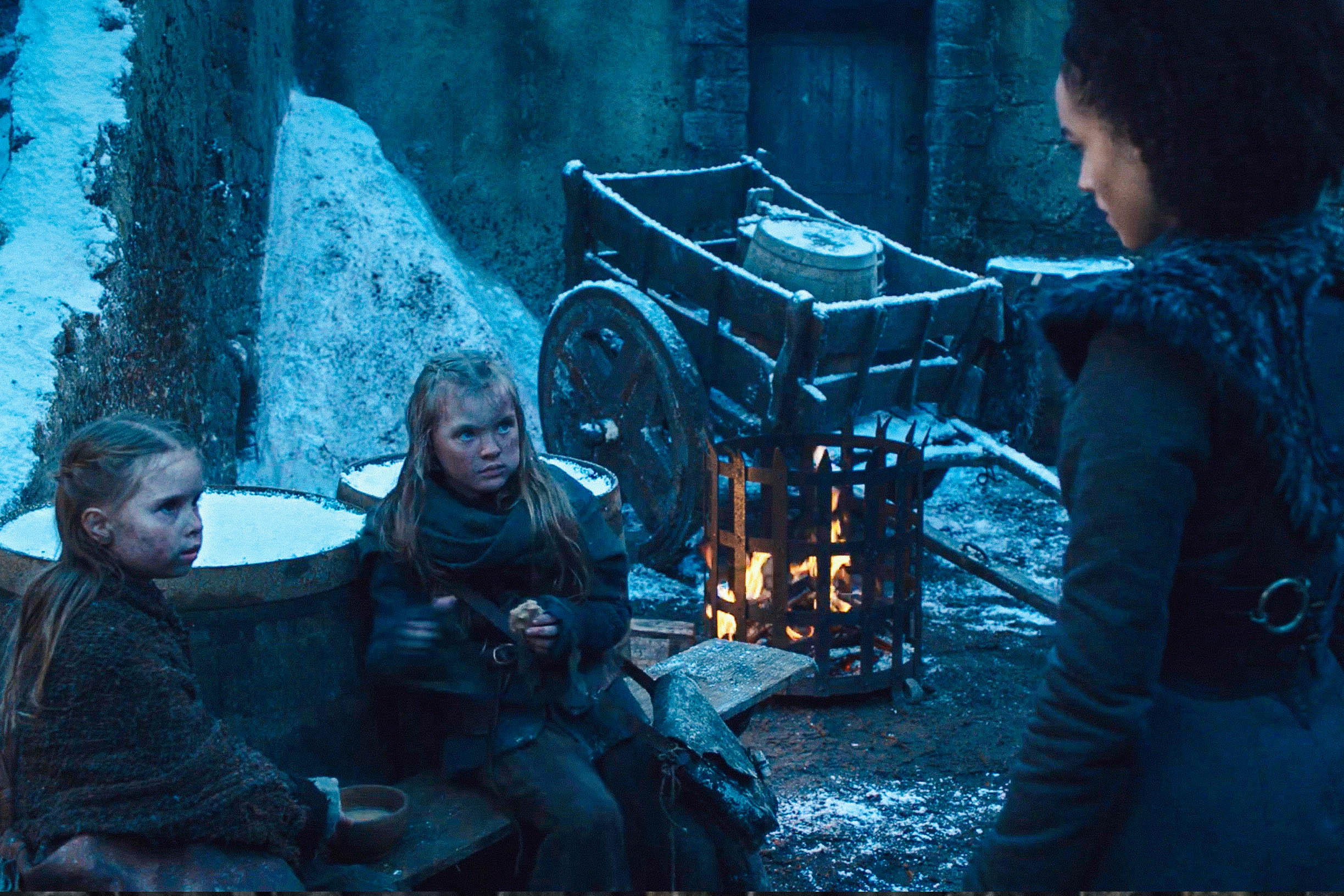 Two young white girls in Winterfell's courtyard look suspiciously at Missandei.