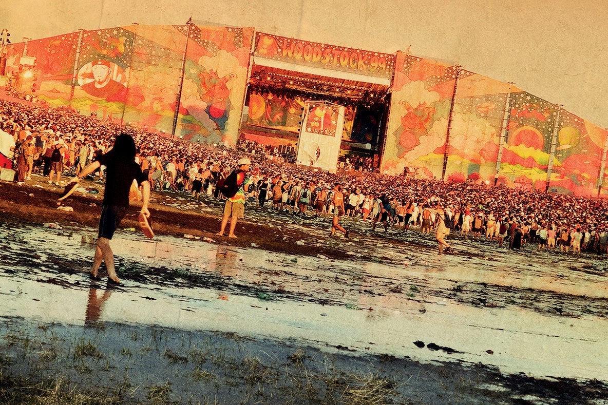 Beyond a mud pit an enormous crowd of people pressed up against a stage at Woodstock ’99