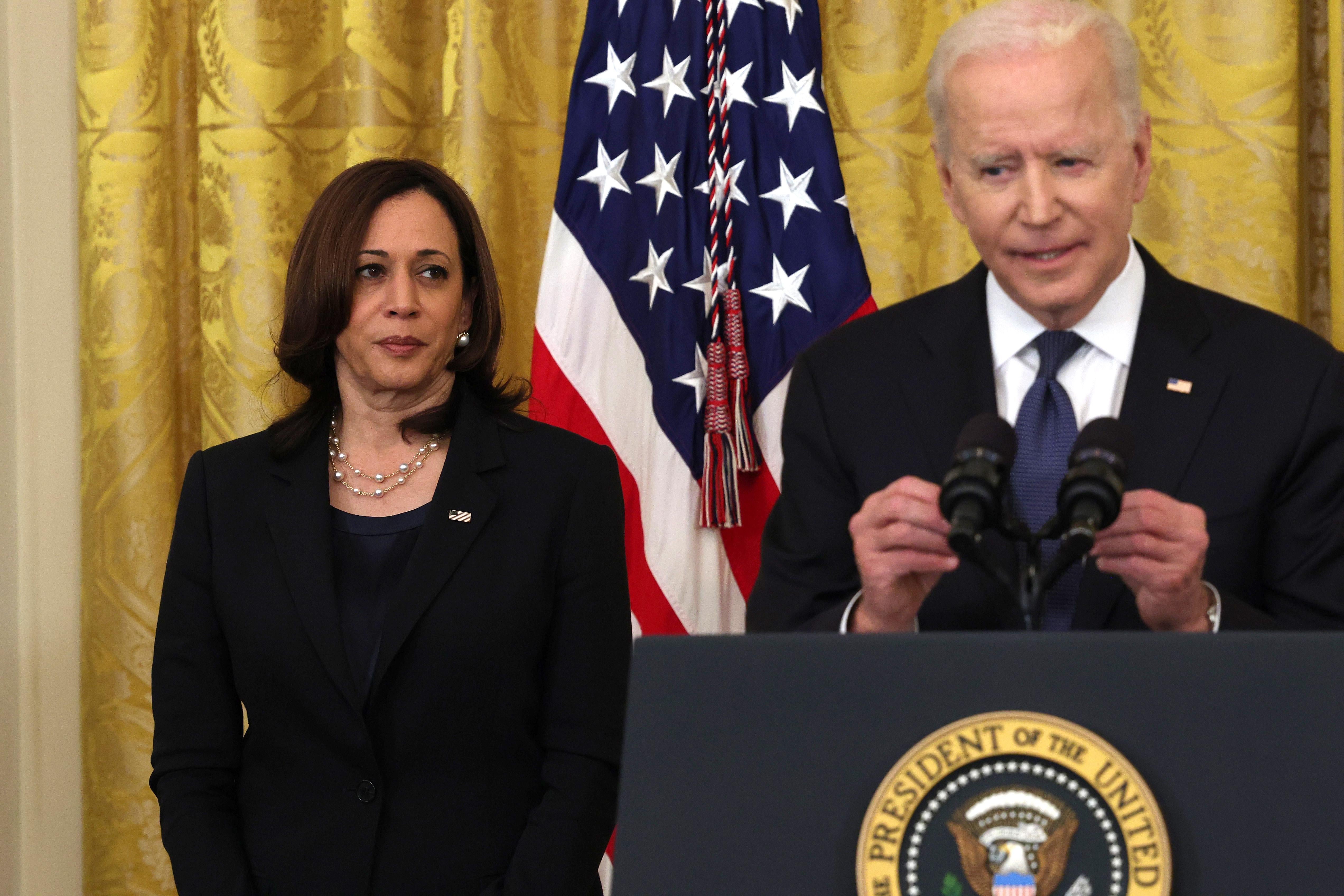 Harris looks at Biden as he speaks at a lectern.