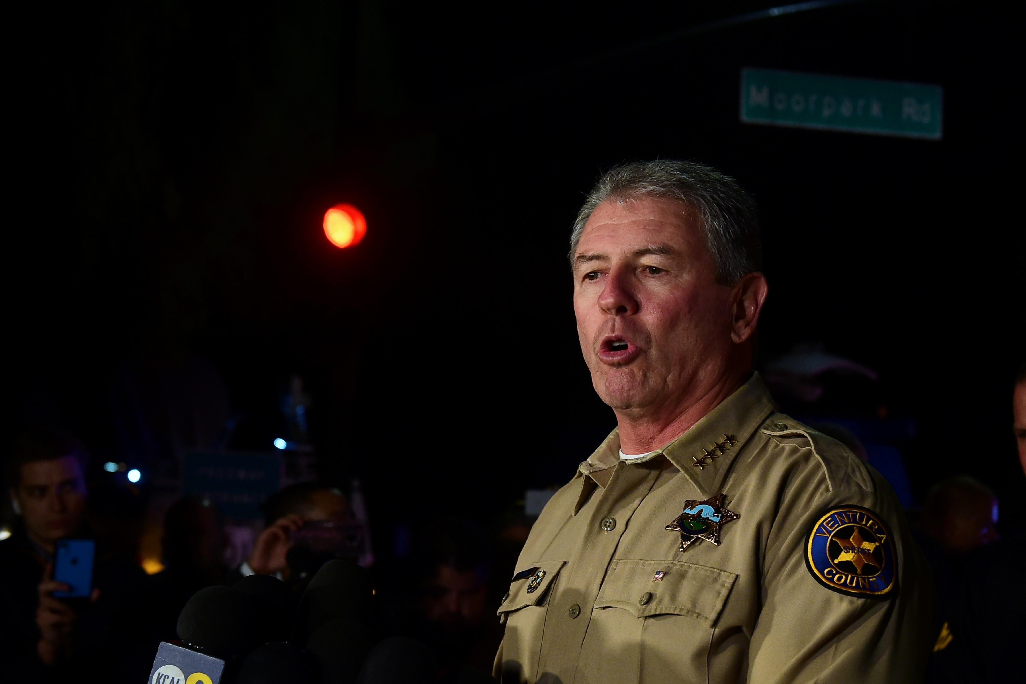 Ventura County Sheriff Geoff Dean speaks. An FBI reporter stands behind him. It is a dark night.