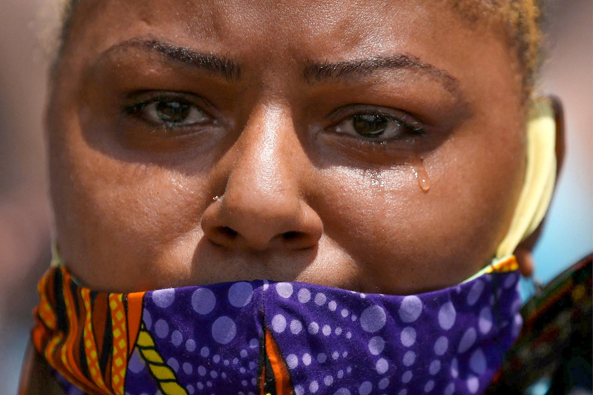 A woman sheds a single tear and wears a purple scarf as a mask.
