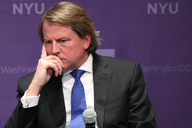 McGahn seated onstage in front of a mic, holding his face and listening.