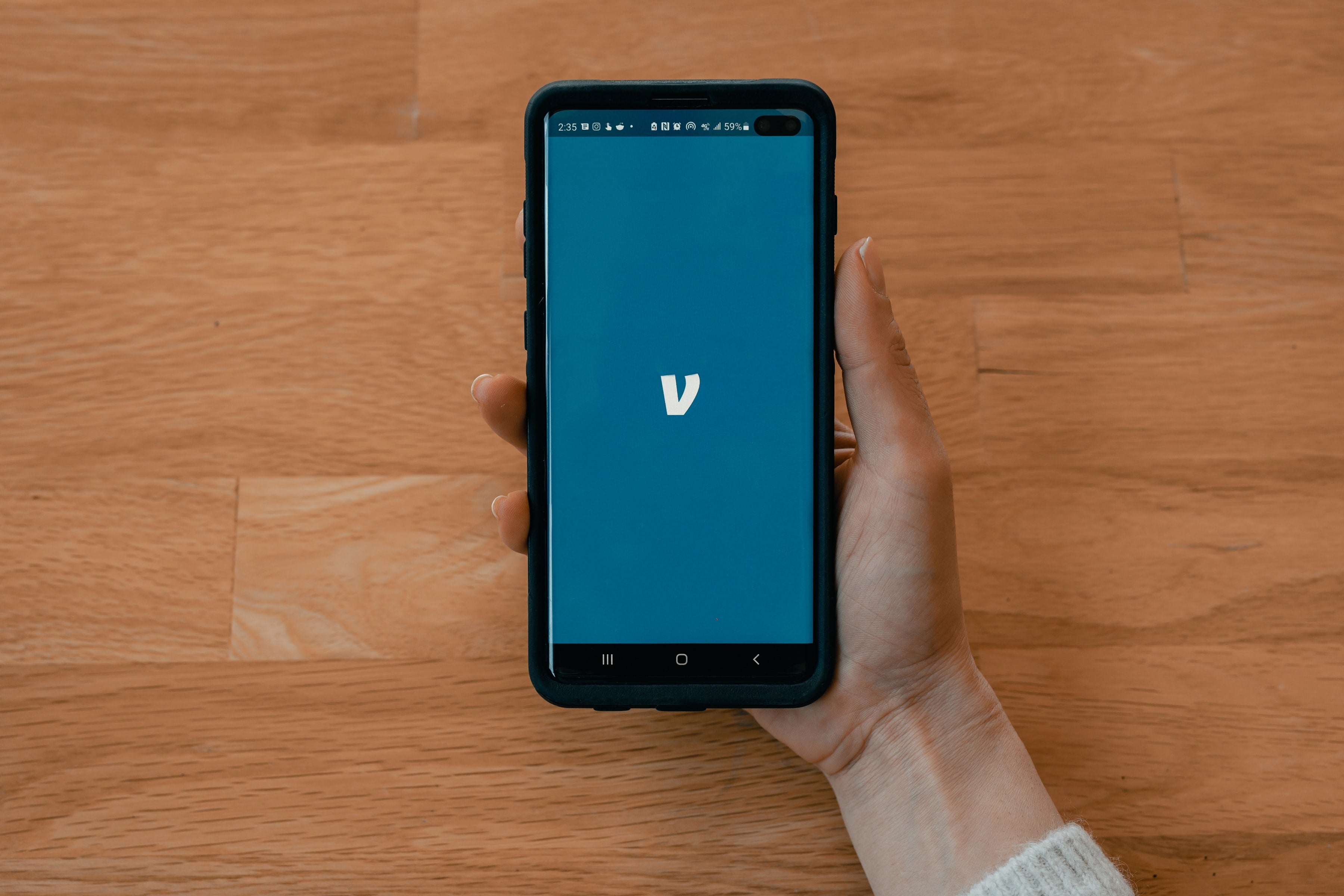A hand holding a black Samsung smart phone showing the Venmo logo.