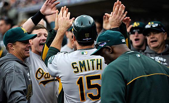 Seth Smith #15 of the Oakland Athletics is congratulated by teammates in the dugout after Smith scored.