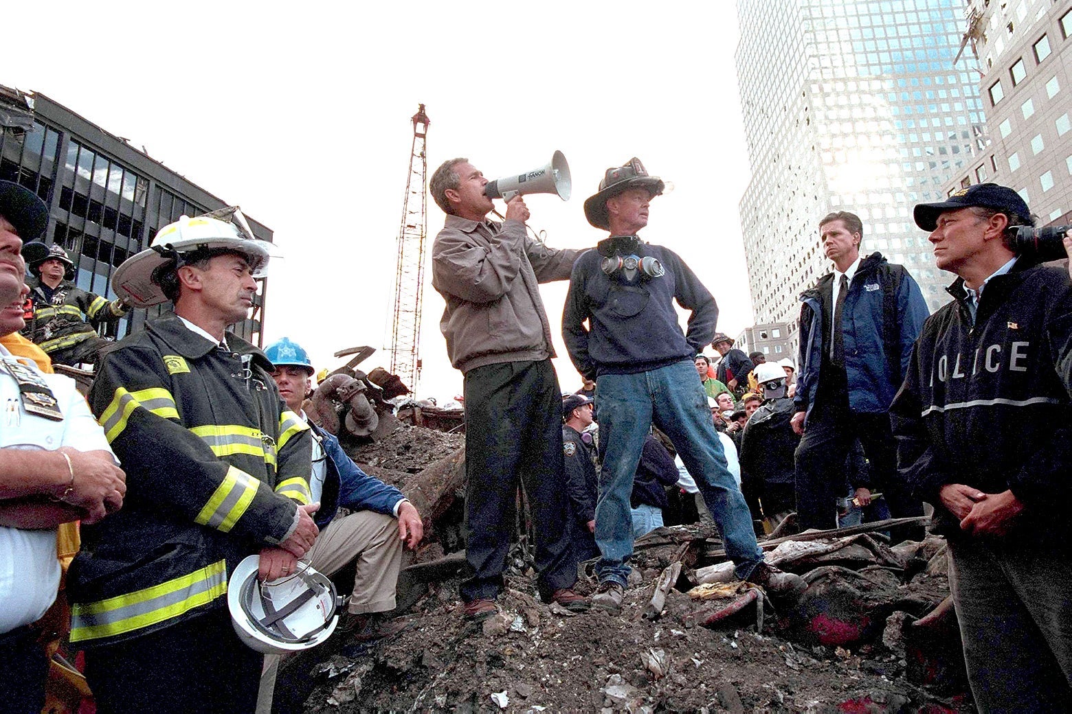 Bush uses a bullhorn as he stands on rubble surrounded by rescue workers, firefighters, and police.