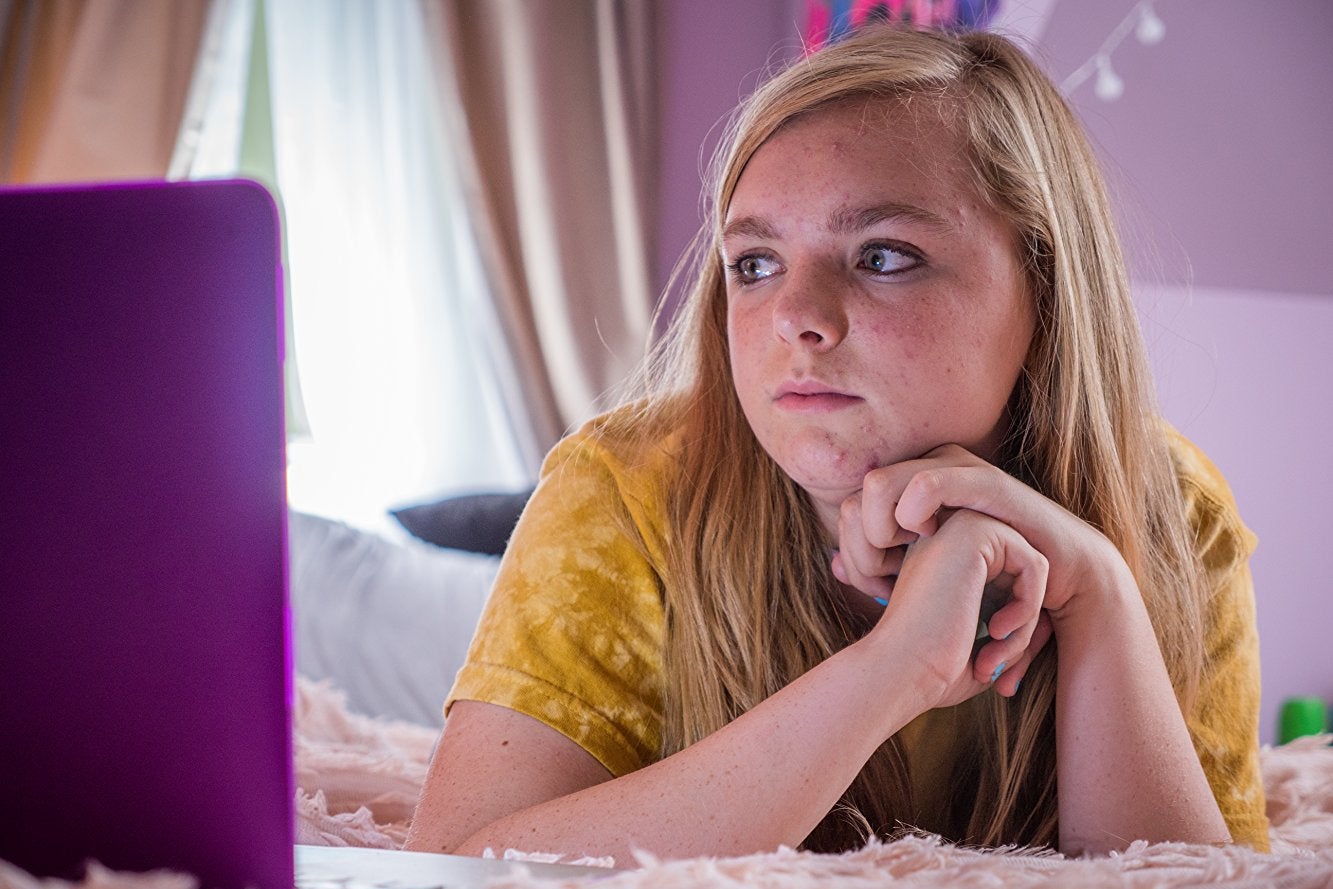 Elsie Fisher looks at a laptop in a purple-decorated room.