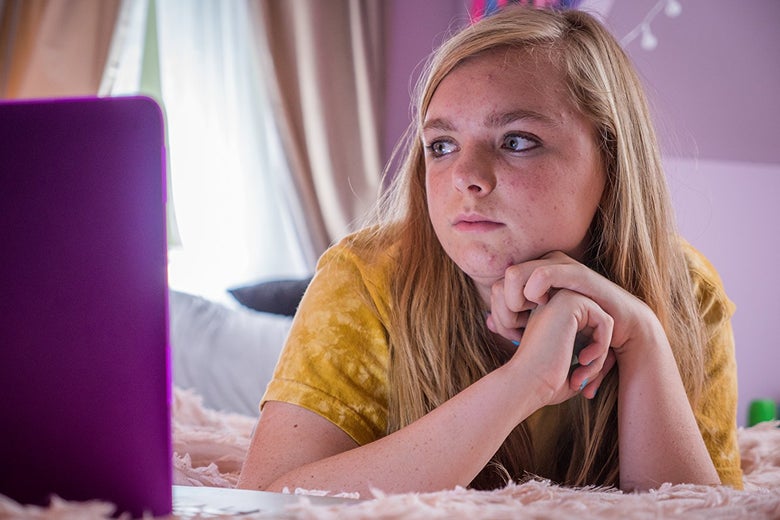 Elsie Fisher looks at a laptop in a purple-decorated room.