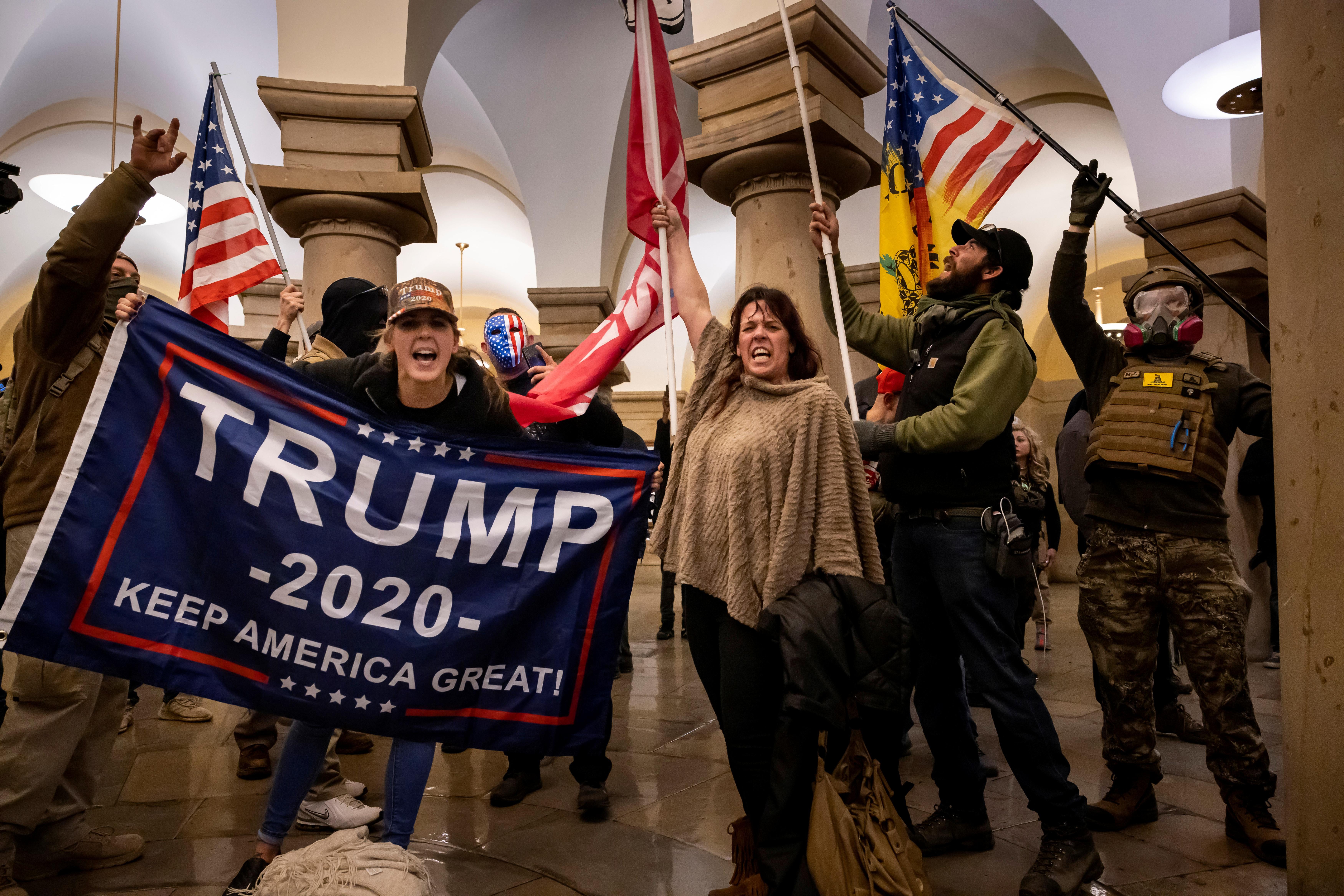 woman yelling while holding a trump flag, a woman holding an American flag, and some dudes cosplaying as militia members inside the Capitol
