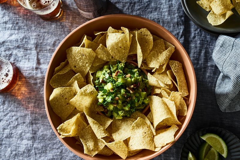 A bowl of tortilla chips, arranged in a circle around a pile of guacamole.