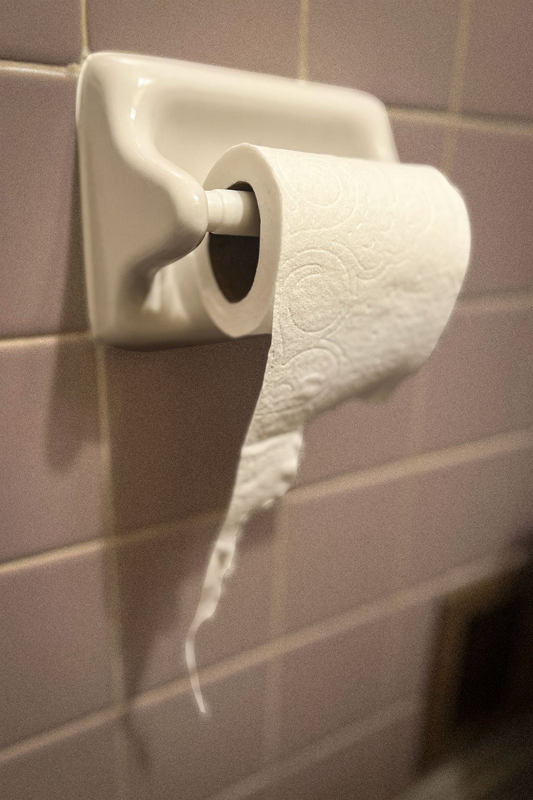 A hanging roll of toilet paper has a weird sideways string from an incomplete tear. 