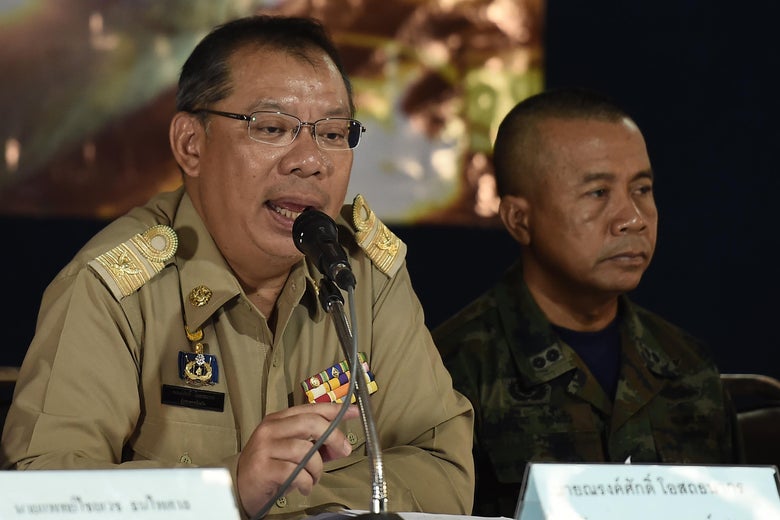 Narongsak Osotthanakorn, wearing glasses and a brown uniform, speaks into a microphone.