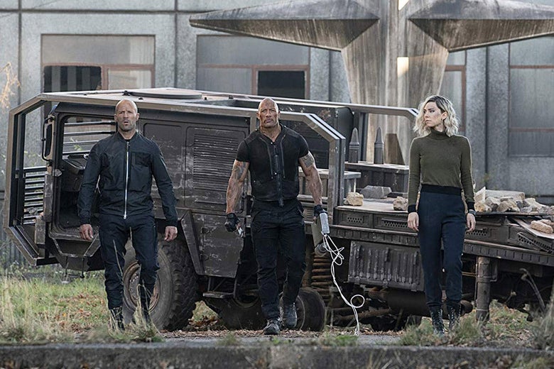 Jason Statham, Dwayne Johnson, and Vanessa Kirby walk toward the camera away from some sort of military vehicle.