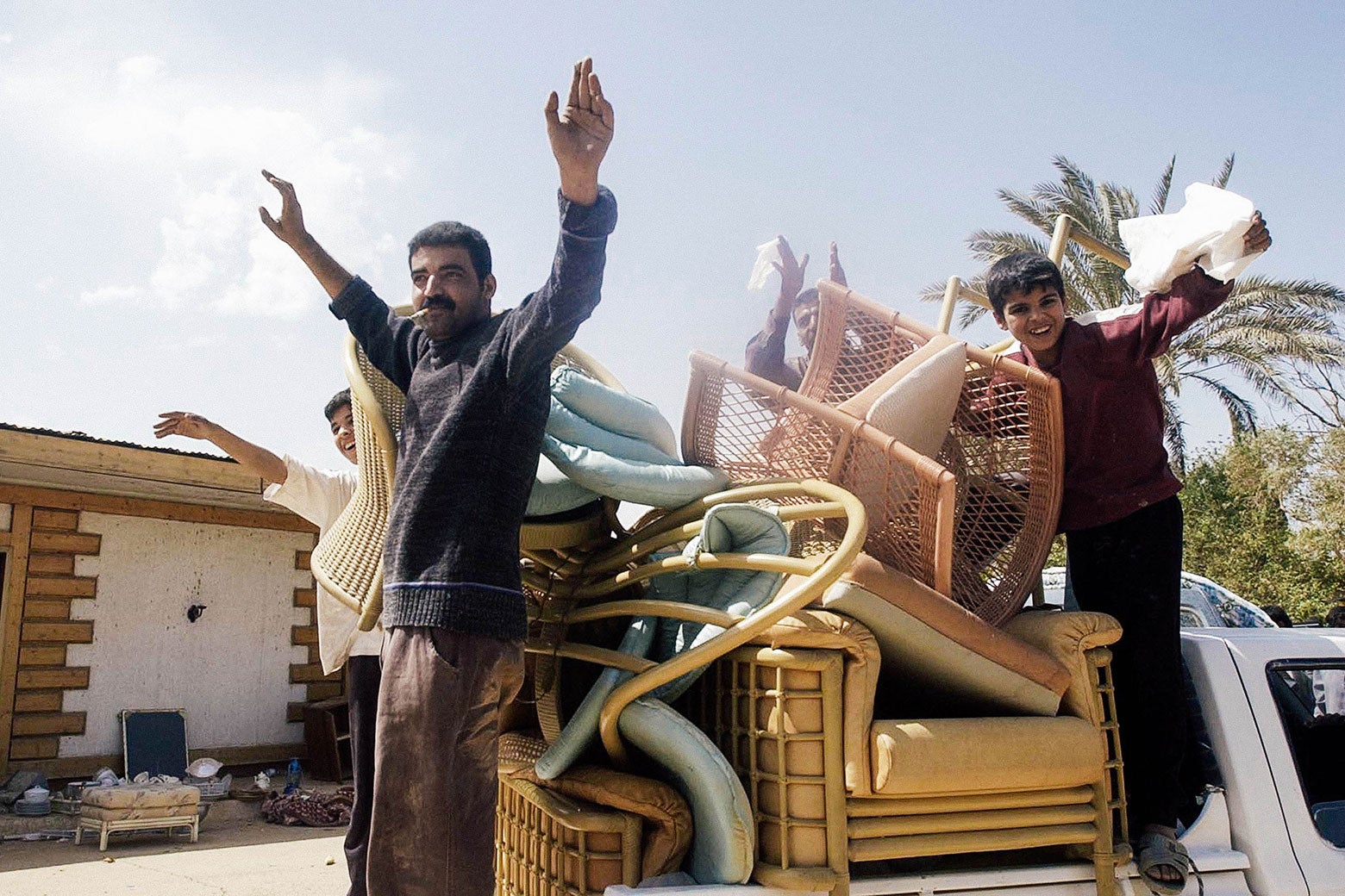 Iraqis stand in the back of a truck piled high with furniture.