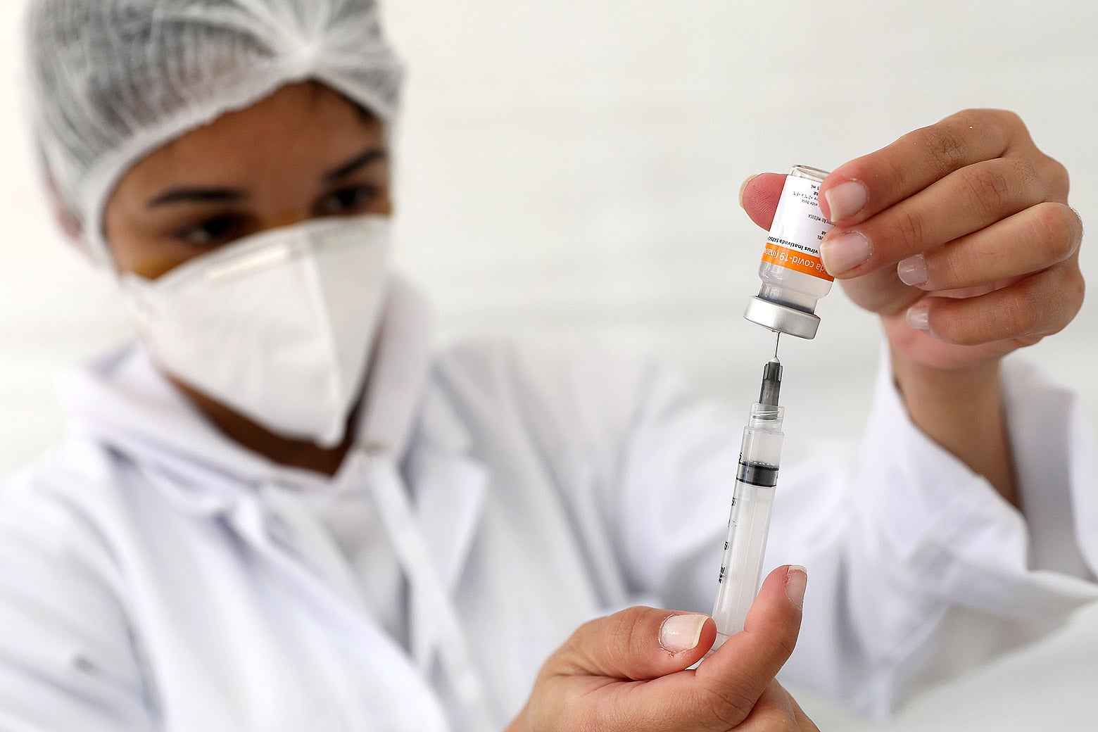 A masked health-care worker, wearing all white, fills a syringe with a vaccine.