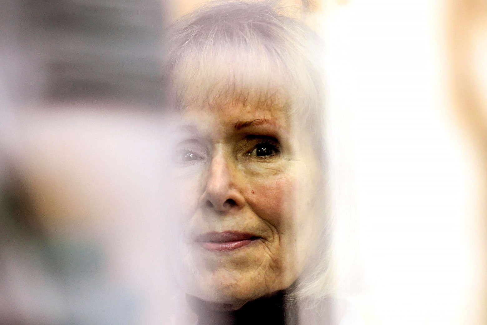 E. Jean Carroll looking at the viewer flanked by blurred images.