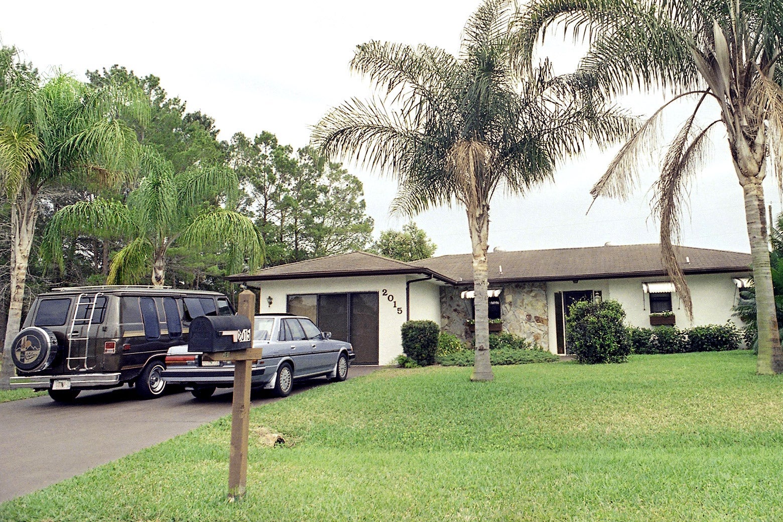 The one-story house has a long yard and two cars parked in the driveway.